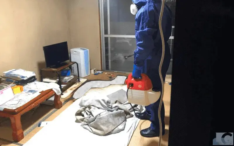 防護服と防護マスクで防備して遺体から出た腐敗体液がこびりつく汚物に消臭剤を噴霧。